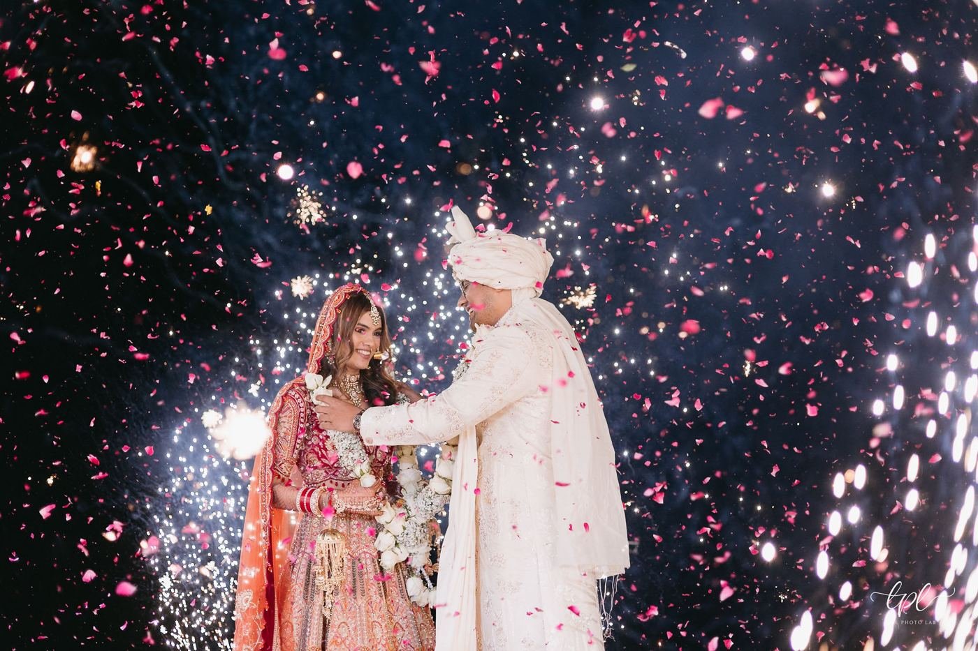 Bride and groom at the varmala under falling rose petals and cold pyros
